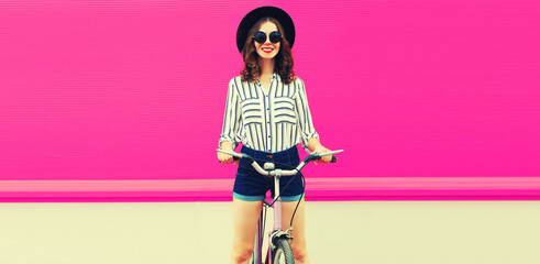 Summer colorful portrait of happy smiling young woman with bicycle in the city on pink background