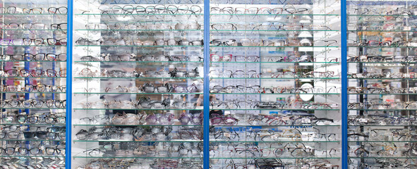 Sunglasses on optics shelves. Large selection of glasses for vision correction. The glasses are laid out on the store's glass shelves in neon lighting.