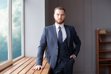 Wall Mural - Serious confident smart handsome businessman in suit looking at camera standing near window in office