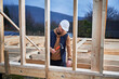 © anatoliy_gleb - Man worker building wooden frame house on pile foundation. Carpenter hammering nail into wooden joist, using hammer. Carpentry concept.