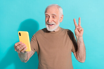 Portrait of handsome trendy cheery grey-haired man taking selfie showing v-sign isolated over bright blue color background