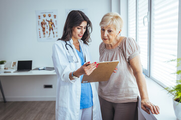 Attractive young female doctor consulting with a patient inside her office at a hospital. Close up of a senior woman having a doctors appointment. A female doctor standing next to female patient