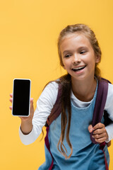 Wall Mural - Positive schoolkid holding backpack and smartphone with blank screen isolated on yellow.