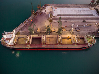 Aerial view of big cargo ship bulk carrier is loaded with grain of wheat in port at sunset