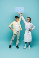 Wall Mural - Smiling multiethnic schoolkids holding speech bubble on blue background.