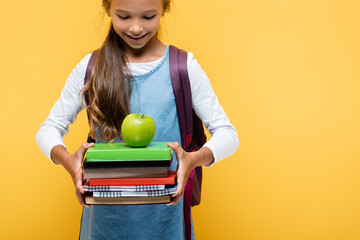 Wall Mural - Smiling schoolchild looking at books and apple isolated on yellow.