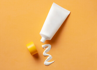 White cosmetic tube with sunscreen cream and squeezed cream texture on orange background.