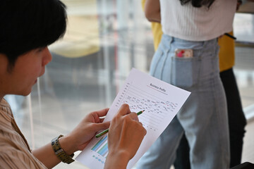 Cropped view of a businessman holding a chart document and working on the document while listening to the presentation in aa]n office, for business and finance concept.