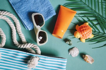 Wall Mural - Summer beach essentials travel packing. Striped bag, sunglasses, orange sunscreen tube, blue towel, turtle toy, palm leaves and seashells. Flat lay vacation photography