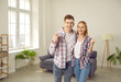 © Studio Romantic - Happy excited newlywed couple celebrate moving into their new home. Portrait of a joyful young family standing in a modern living room interior, hugging, fist pumping and smiling. Buying house concept