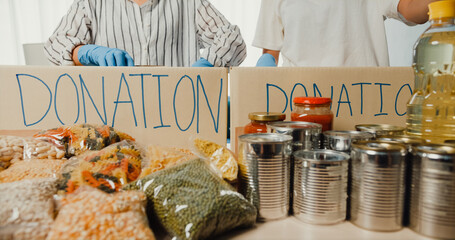 Group of young Asia teenage girl volunteer wear gloves packing food and drink donation into donations paper boxes while work in charitable foundation. Social worker, food bank and coronavirus concept.