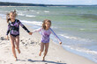 Cheerful little girls sisters play on the seashore.