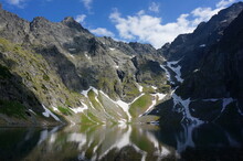 Black Lake Below Mount Rysy (Czarny Staw Pod Rysami) At 1583 Meters Above Sea Level. Snow White Streaks Are Reflected In The Water, June 2022. Tatra Mountains, Poland.