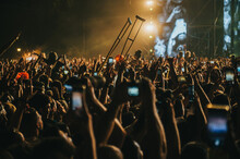 People In A Crowd Of A Music Concert Using Their Smartphones And Someone Holding Crutches