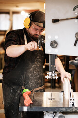 Vertical serious and tired mature male worker, carpenter in protective uniform use wood cutting machine. Small business