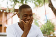 © Юля Бурмистрова - Smiling, laughing and cheerful african american man covering his face by hand in the street outdoors. Watching something funny. Getting new job, successful interview. Freelance worker in his weekend.