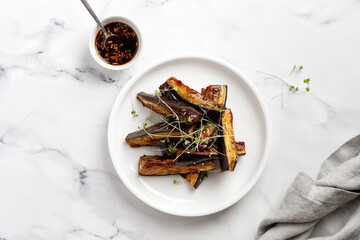 Hot spicy Glazed Fried eggplant with sauce, honey, microgreens on white plate and marble background, delicious vegetarian Chinese food dish, top view.