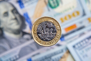 British one pound coin close up and blurred hunder dollar banknotes on the background. Concept for inflation. Not a montage, real photo.