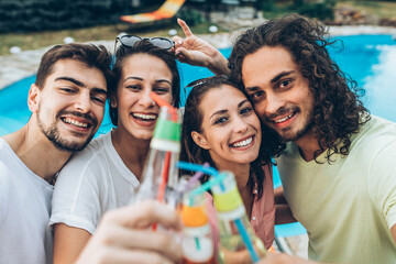 Wall Mural - A group of young people refreshing by the swimming pool and toasting together with cold drinks.	