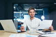 © Liubomir - Young handsome man businessman, director, boss signs and concludes a successful business deal. Holds documents in his hands. He waits at his desk in the office, smiling