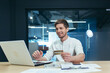 © Liubomir - A young man is sitting in the office at his desk, holding a credit card, working on a laptop. Makes orders online, pays bills