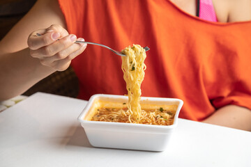 A woman eats instant noodles. Hot noodles on a fork.. White background. Noodles in the mouth and hanging into a plate