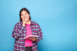 © Lux Images - Young curvy latina woman touching chin, thinking and holding notepad to write plans. Indoor studio shot isolated on blue background.
