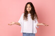 Portrait of annoyed frustrated little girl wearing white T-shirt standing with raised hands and indignant face asking why, annoyed by problem. Indoor studio shot isolated on pink background.