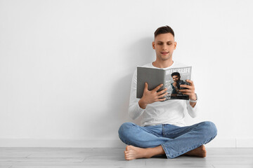 Sticker - Young barefoot man reading magazine near light wall