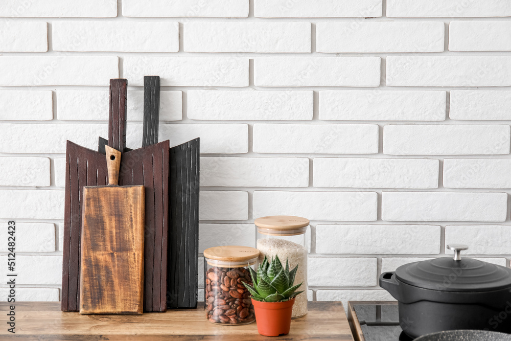 Cutting boards, houseplant and utensils on kitchen counters near white brick wall