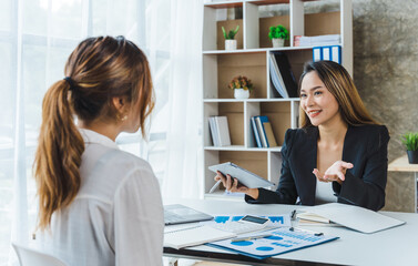 Two young Asian business female people explaining a list of collaboration using document and taking notes at the office.