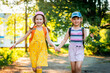 Two funny little girls of different races, in dresses and baseball caps, with a bouquet of wildflowers, run and laugh. Best friends like to chat and walk in the fresh air at sunset. Summer holidays