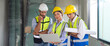 © chadchai - Young architect pointing at laptop computer monitor explain to foreman and engineer about a floor plan. Everyone wear helmet and safety vest. Work environment at construction site of housing project.