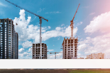 blank white long information banner fixed on construction site hoarding under working cranes against