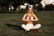 © Rabizo Anatolii - Praying and meditation in lotus position online with laptop. Fit girl is sitting and meditating on the grass in the park.