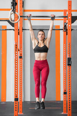 Fit athletic woman doing a dead hang in a Crossfit gym