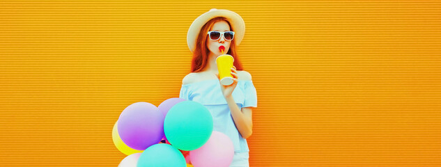 Summer portrait of happy woman drinking fresh juice with colorful balloons having fun wearing straw hat on orange background, blank copy space for advertising text