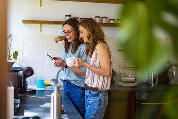 Two women using mobile phone in the kitchen at home
