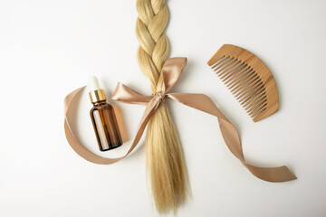 Wall Mural - A natural oil or serum for hair care treatment and a tress of blonde hair with bow lying on a white background