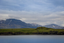 Majestic Icelandic Landscape Of Horizontal Stripes Of Body Of Water, Grass Colored Hills And Snow Covered Mountains