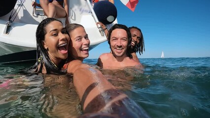 Wall Mural - Happy multiracial friends streaming live video swimming in the sea with sail boat in background 