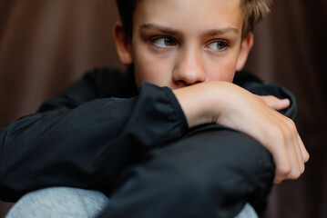 Portrait of blonde teenage boy on dark background outdoor. Low key close up shot of a young teen boy, adolescence. Selective focus. Loneliness, sadness, adolescent anxiety, emotional