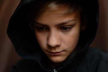 Portrait of blonde teenage boy on dark background indoor. Low key close up shot of a young teen boy, adolescence. Selective focus. Loneliness, sadness, adolescent anxiety, emotional