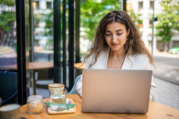 Young smiling brunette business woman in stylish smart dress working on laptop in cafe at street of Prague