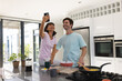 © Wavebreak Media - Cheerful asian young woman taking selfie with caucasian boyfriend making breakfast in kitchen