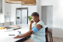 African American Senior Woman With Short Hair Checking Blood Pressure With Gauge At Kitchen Island