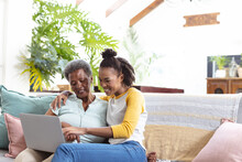 Cheerful African American Young Daughter With Senior Mother Using Laptop While Relaxing On Sofa