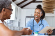© Wavebreak Media - Smiling african american doctor holding digital pc giving medicines to senior patient at home