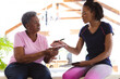 © Wavebreak Media - African american senior woman showing hand to female physiotherapist while sitting on table at home