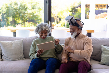 Cheerful african american senior friends using virtual reality simulator and digital pc on sofa